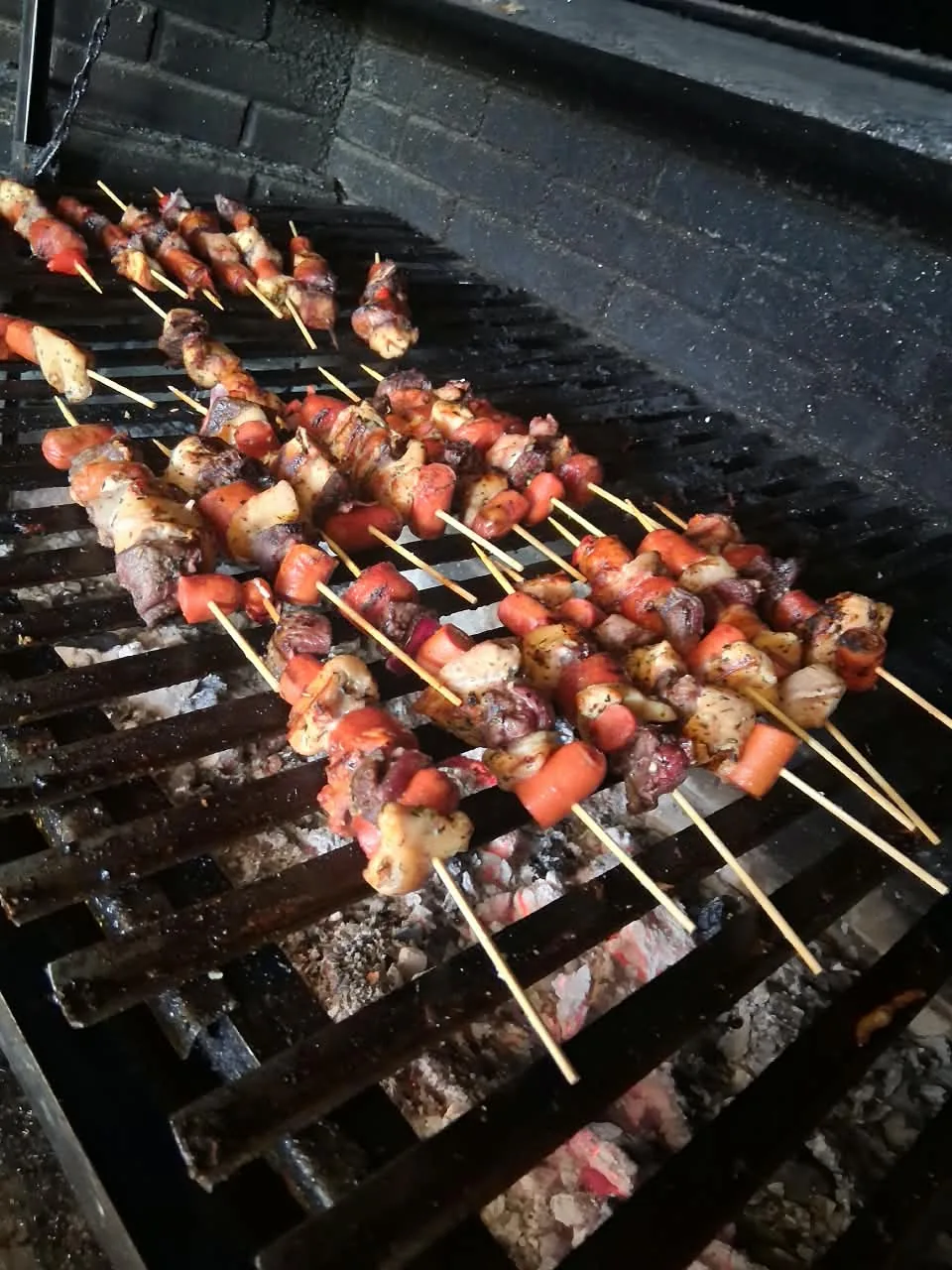 Brochetas de carne, pollo y vienesa sobre la parrilla a las brasas